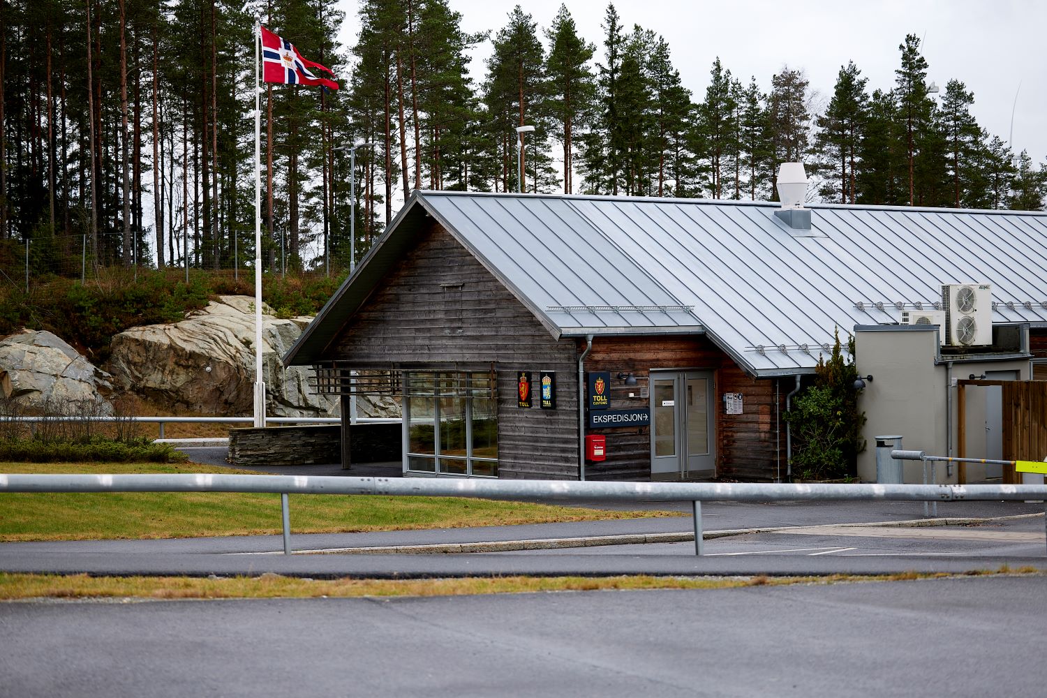 Foto av et tollsted. Tollstedet er bygget i tre, og har etatsemblem til både svensk og norsk toll ved inngangsdøren. Utenfor tollstedet flagges det med norsk vimpel.